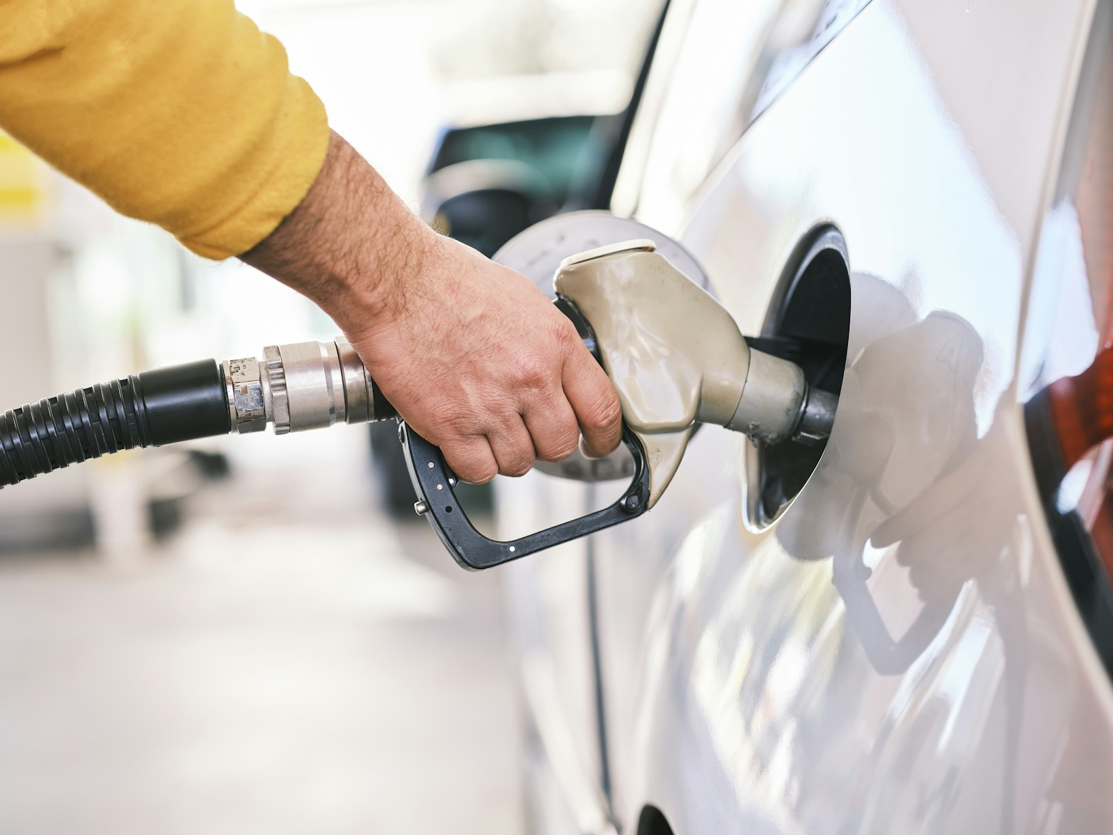 Automobilist met een vulpistool bij de tankopening van een auto
