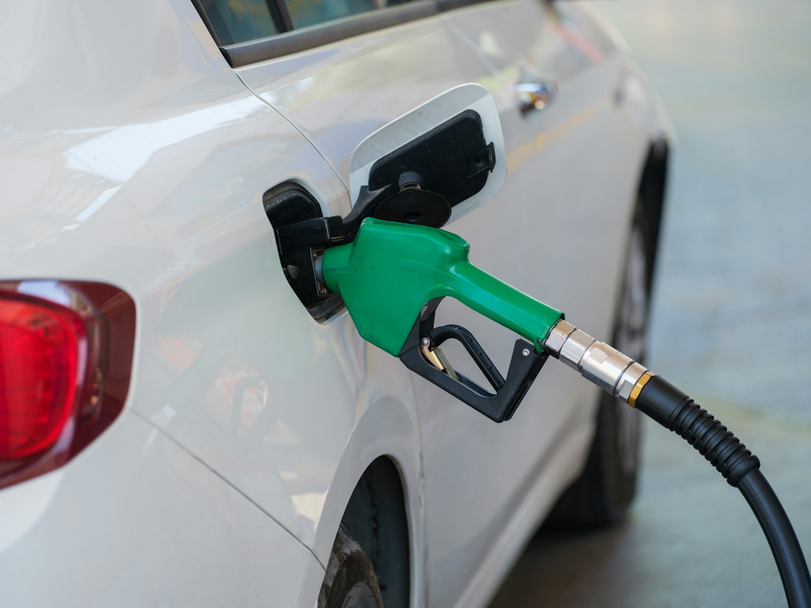 Groen vulpistool voor Euro 95 in de tankopening van een witte auto